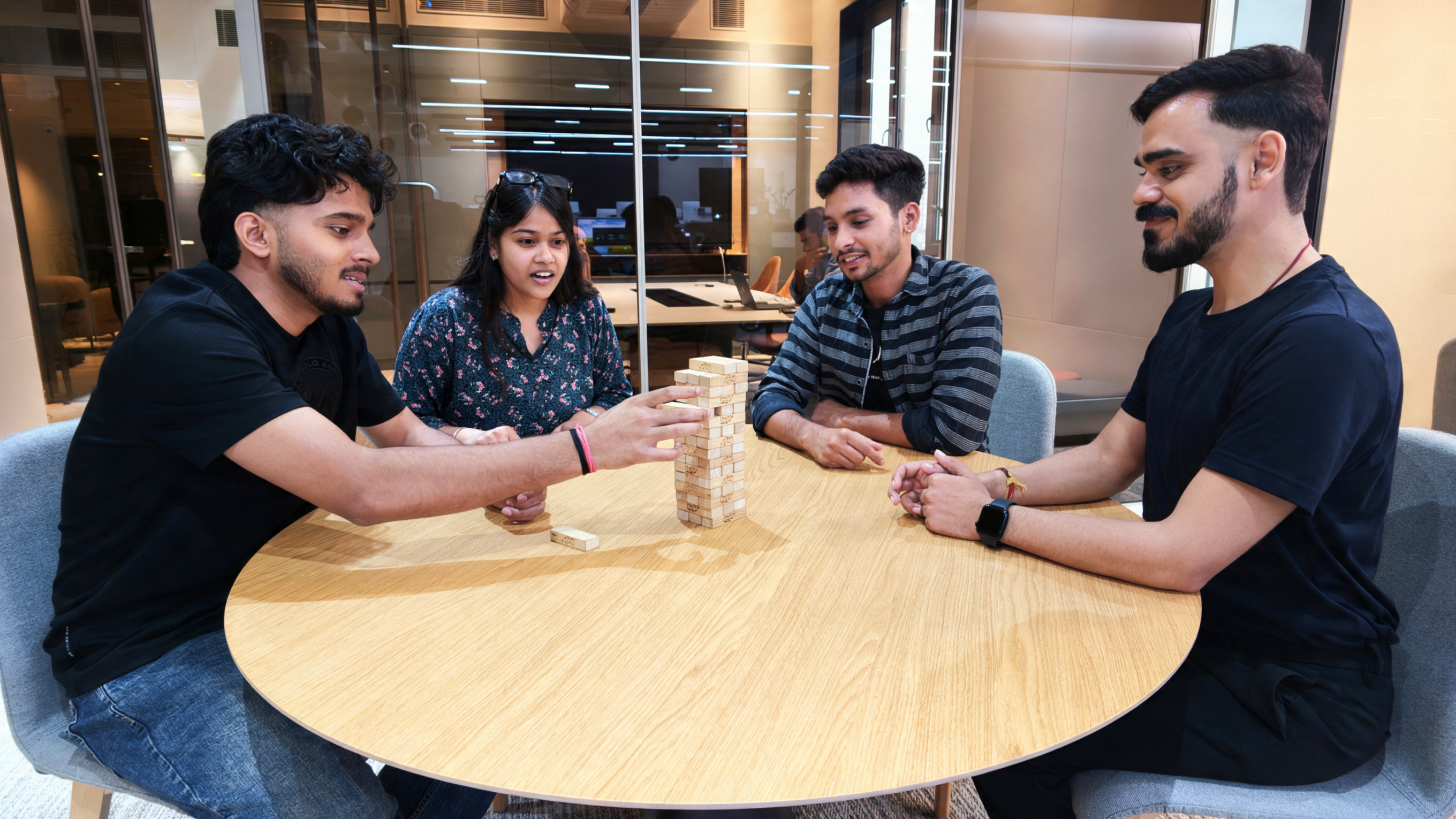 Four MoreTasks colleagues playing Jenga around a table in the office