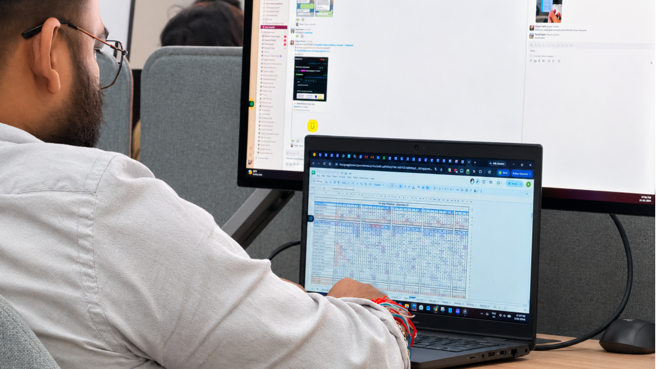 A MoreTasks colleague working across a spreadsheet and a chat window at a dual-screen desk